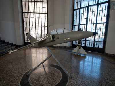 Da qui passiamo all�interno di un�ala della struttura, per ritrovarci in un grande atrio con il pavimento in marmo grigio sul quale campeggia una riproduzione del caccia Amx International, noto anche come �Ghibli�